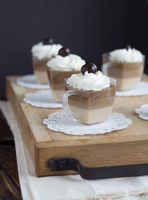 there are four cups with desserts in them on the wooden tray, ready to be eaten