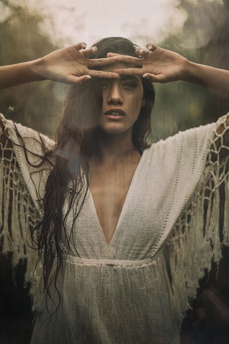 a woman holding her hands over her head in the middle of an image with trees behind her