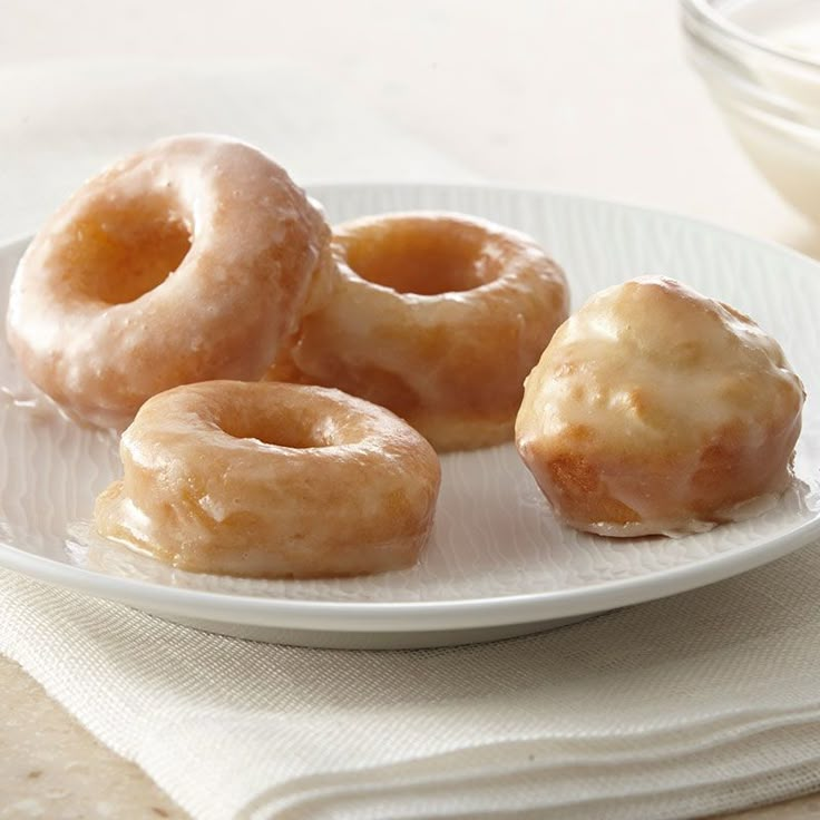 four glazed doughnuts on a plate next to a bowl of yogurt