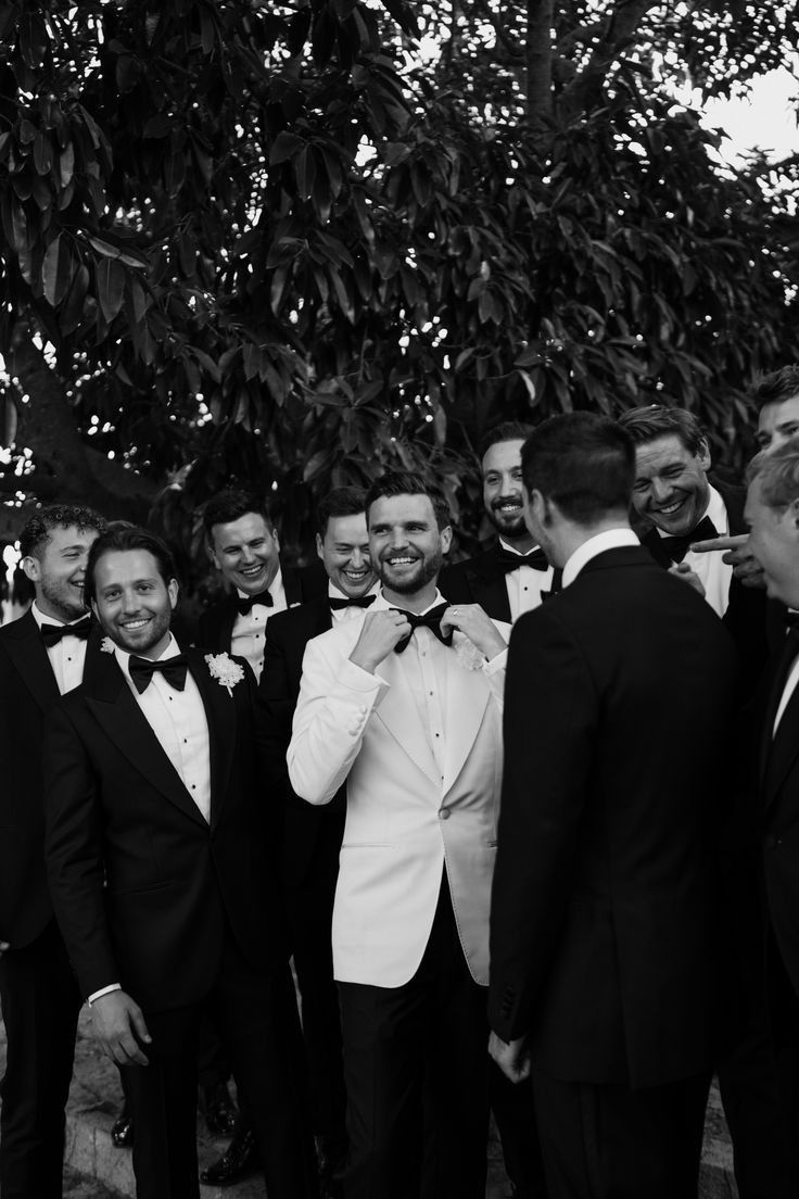 a group of men standing next to each other wearing suits and bow ties in front of a tree