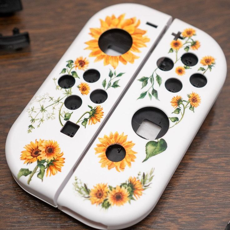 a white cell phone with sunflowers painted on the front and back sides, sitting on a wooden table