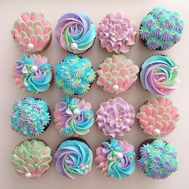 cupcakes decorated in pastel colors are arranged on a white surface with pearls