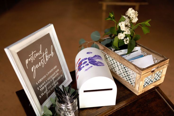 a wooden table topped with a mailbox and vase filled with flowers next to a sign