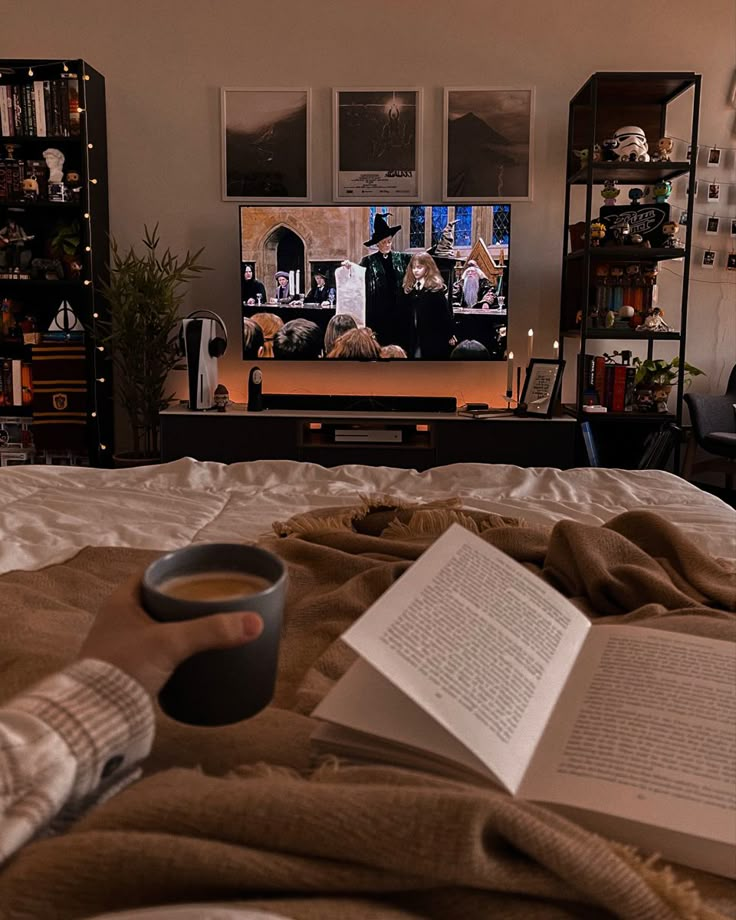 an open book on a bed with a cup of coffee in front of the tv