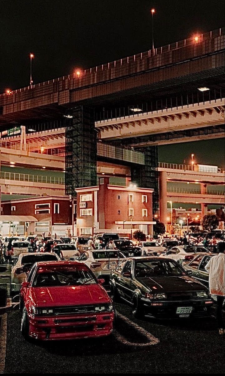 many cars are parked in a parking lot near an overpass at night with lights on