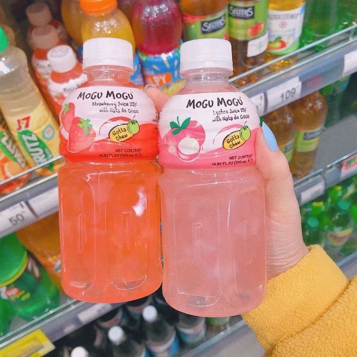 two bottles of soda are being held in front of a refrigerator full of fruit juice