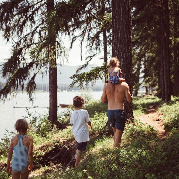 three people are walking in the woods by the water with their backs turned to the camera