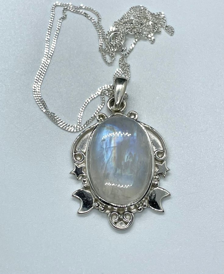 This enchanting pendant showcases a mesmerizing rainbow moonstone with an iridescent glow, set in a beautifully detailed sterling silver setting adorned with celestial stars and a crescent moon. Suspended on a 20" sterling silver chain, this piece captures the magic of the night sky, making it a perfect gift for dreamers and stargazers. This pendant is approximately 1 7/8" long and 1" wide. (not including the bail) Known for its soothing energy and ability to restore balance, the rainbow moonsto Mystical Iridescent Moonstone Necklace, Celestial Moonstone Cabochon Jewelry, Celestial Silver Moonstone Necklace, Silver Celestial Moonstone Necklace, Mystical Silver Moonstone Necklace, Mystical Moonstone Necklace With Sun And Moon Design, Iridescent Moonstone Gemstone Necklaces, Mystical White Moonstone Necklaces, Iridescent Moonstone Gemstone Necklace