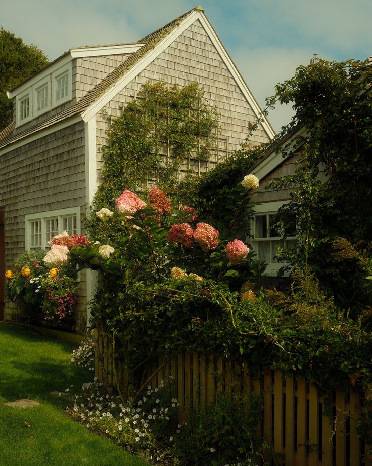 a house that is next to a fence with flowers growing on the top of it