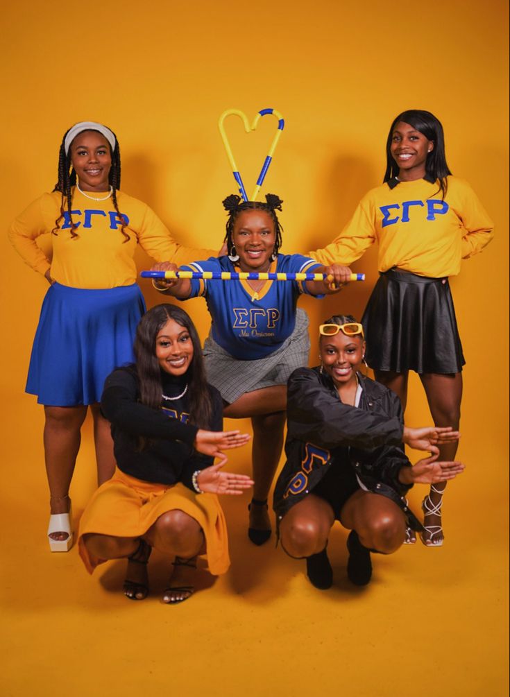 a group of young women posing for a photo in front of a yellow background wearing cheerleader shirts