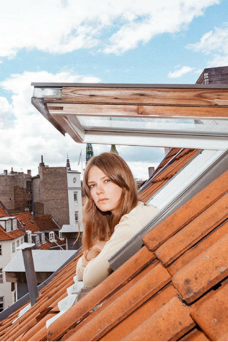 a woman standing on top of a roof looking at the camera with buildings in the background