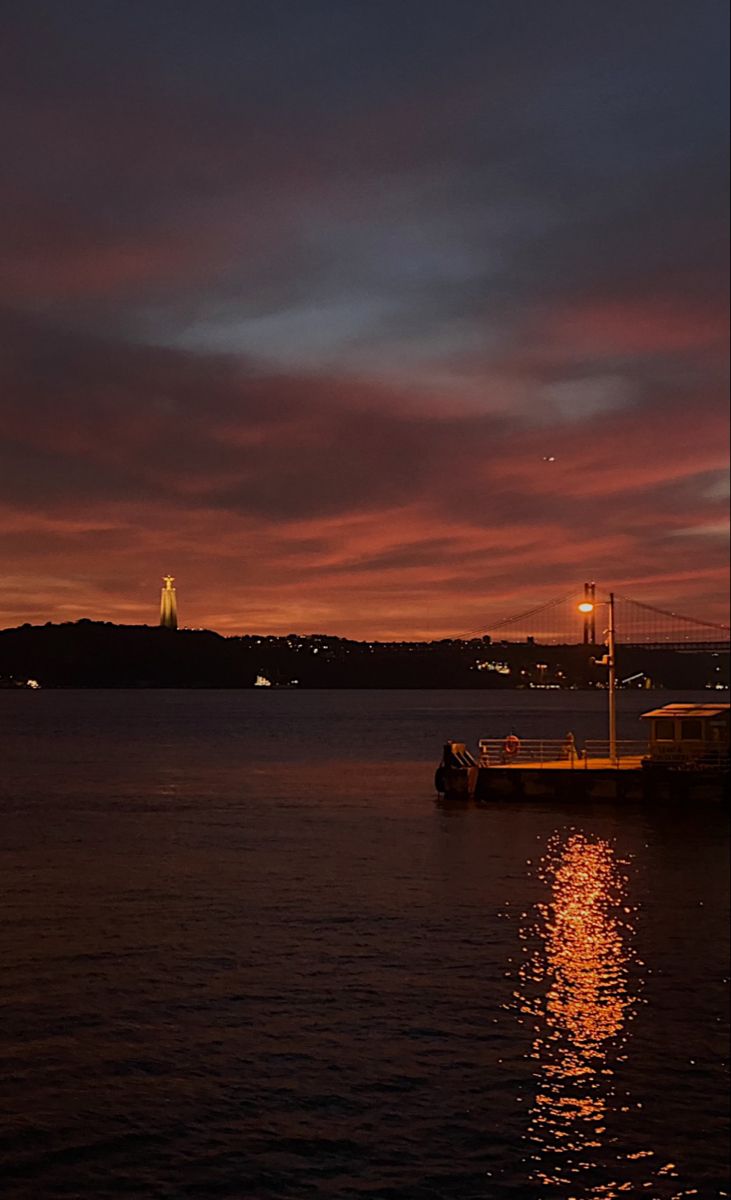 the sun is setting over the water and some boats are out on the water at night