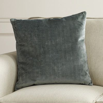 a green velvet pillow sitting on top of a white couch next to a wooden table