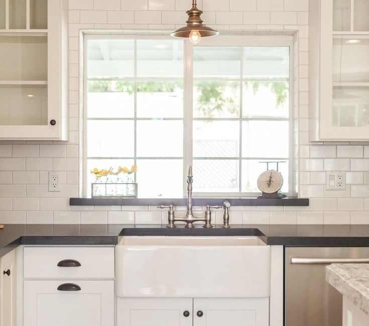 a kitchen with white cabinets and black counter tops is pictured in this image, there are two windows above the sink