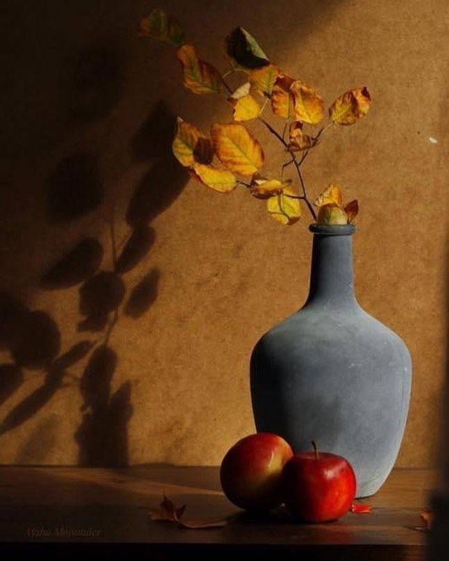 a blue vase sitting on top of a table next to two apples and a plant