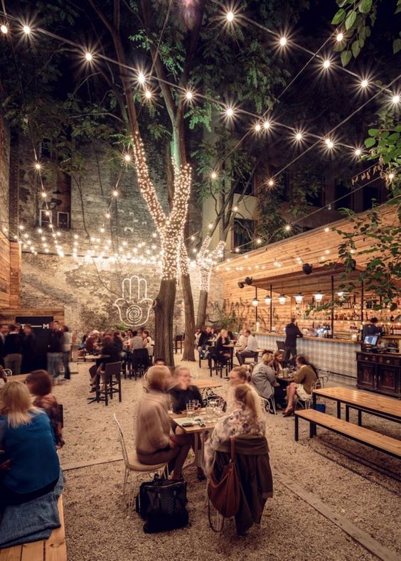 people are sitting at tables in an outdoor area with string lights strung over the trees