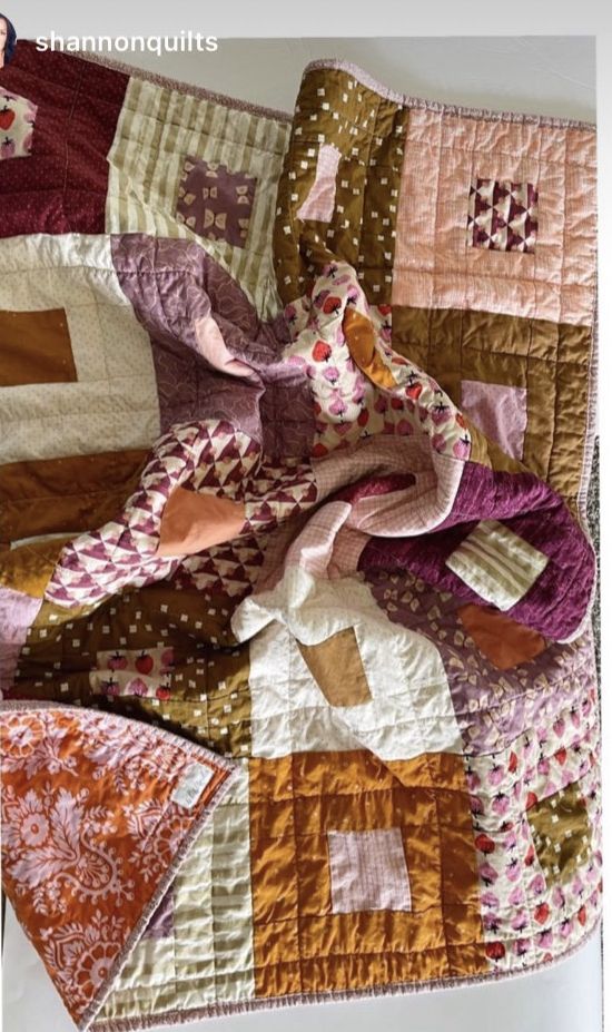 an old quilt is laying on top of a tablecloth with many different colors and patterns