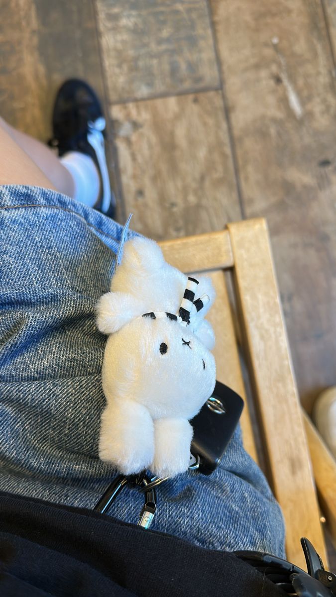 a white stuffed animal sitting on top of a person's lap in front of a wooden floor