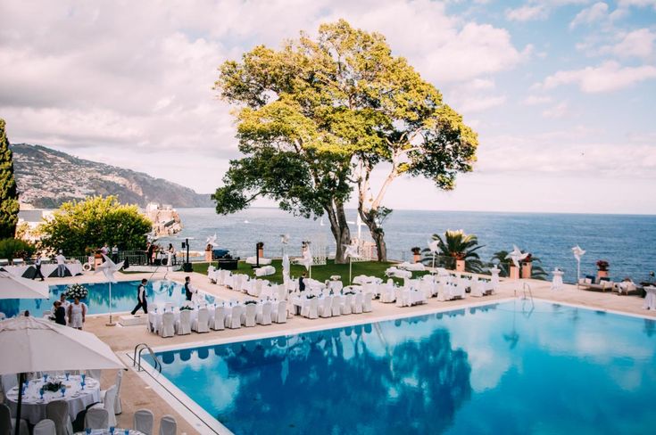 an outdoor pool with tables and chairs set up for a wedding party next to the ocean