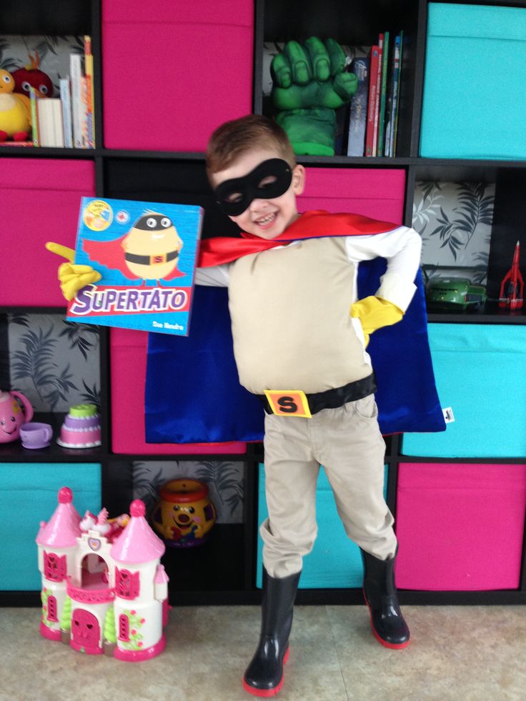 a young boy dressed up as a super hero standing in front of a bookcase