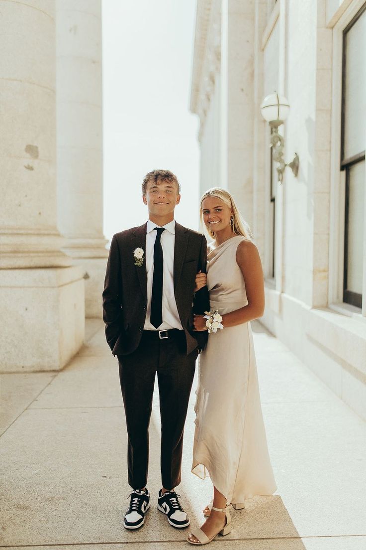 a man in a suit and tie standing next to a woman wearing a white dress