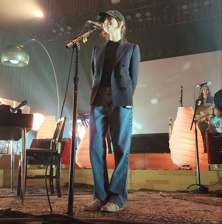 a woman standing in front of a microphone on top of a stage with other people