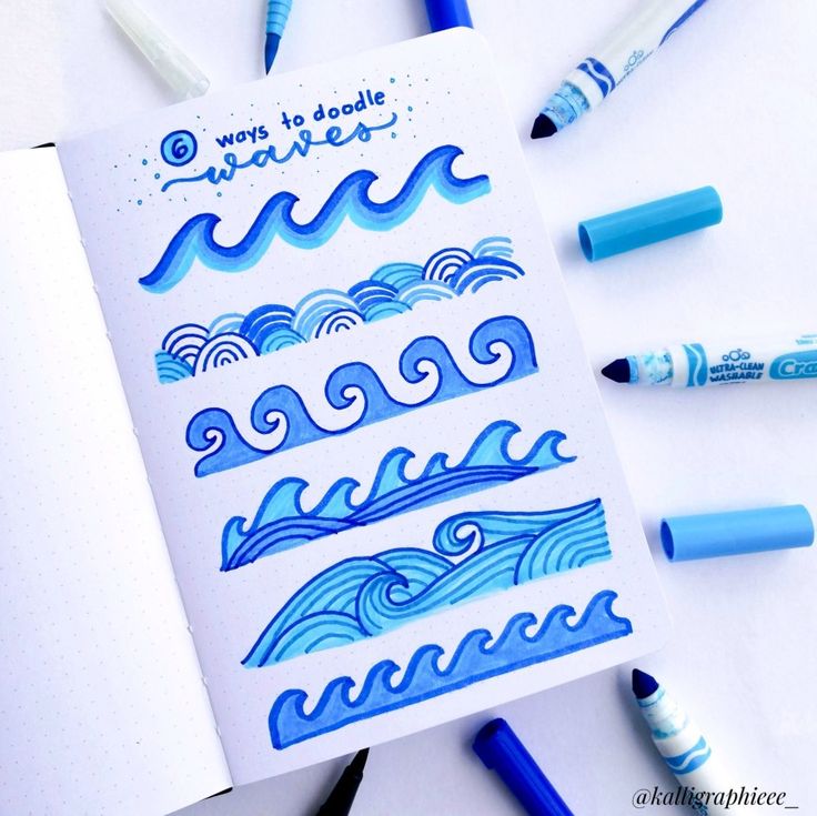 some pens are laying on top of an open notebook with blue water and waves drawn on it