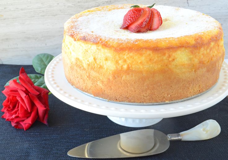 a cake sitting on top of a white plate next to a knife and red rose