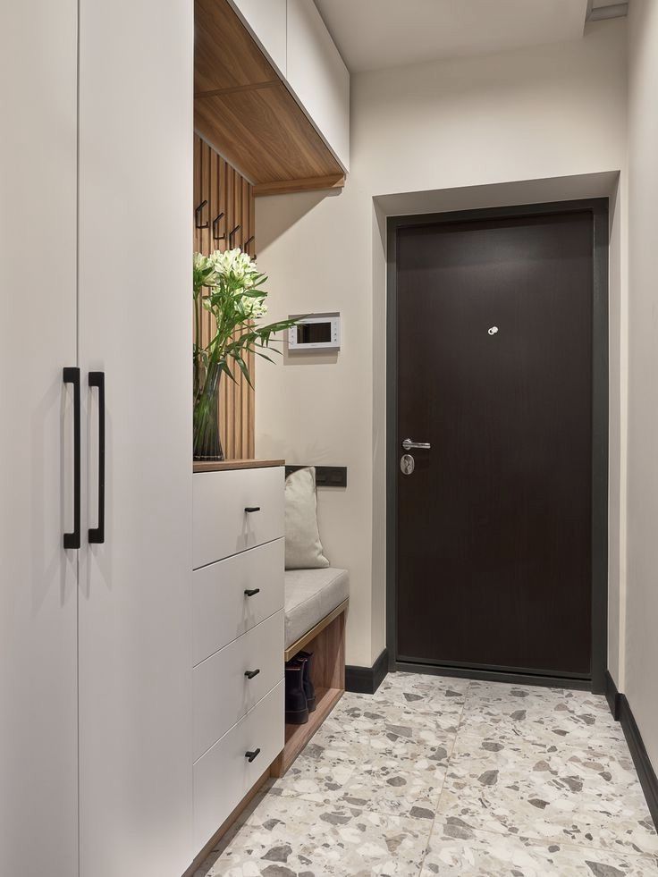 an entryway with white cabinets and drawers in front of a black door that has a plant on it