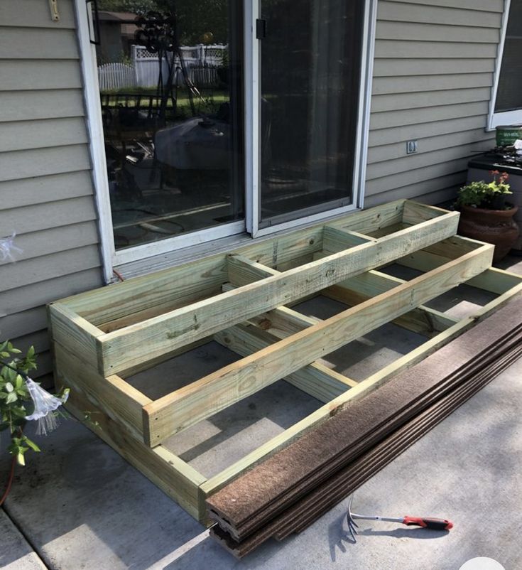 a wooden bench sitting in front of a window on top of a cement floor next to a potted plant