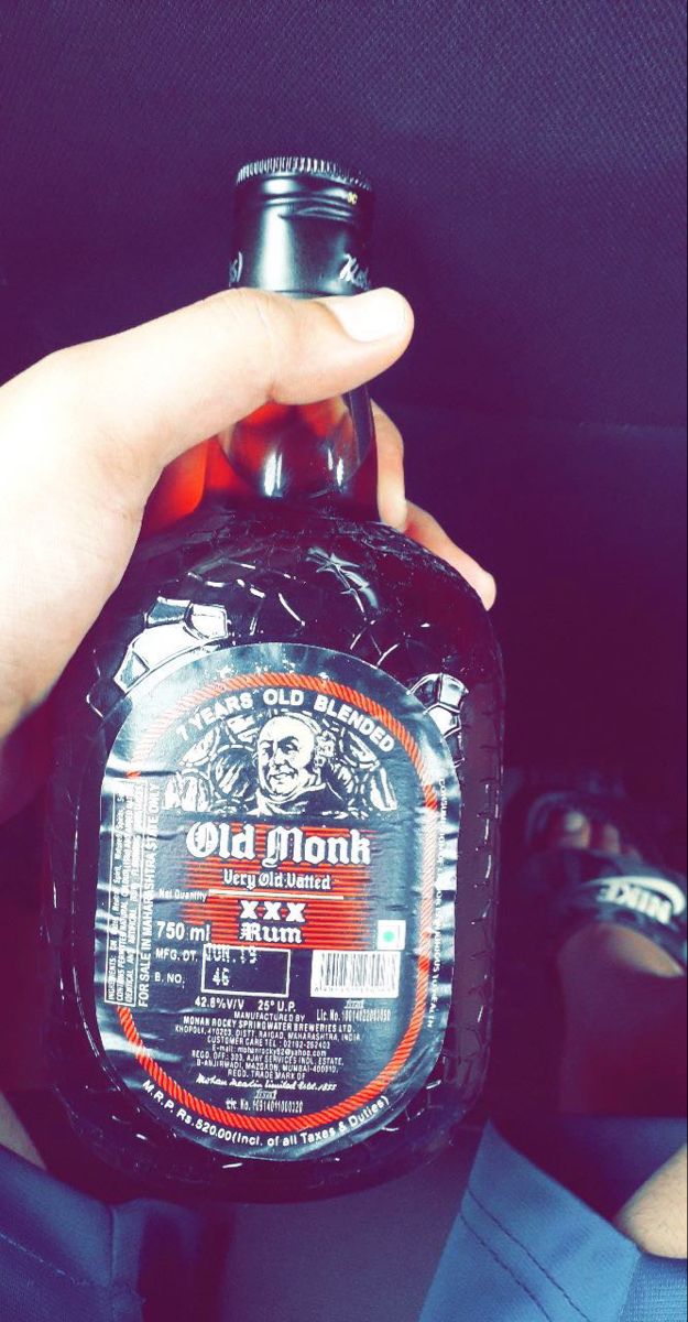 a person holding up a bottle of old monk beer in their lap, with the label on it