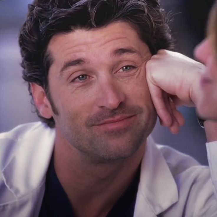 a close up of a person wearing a lab coat and smiling with his hand on his head