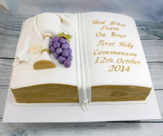 a book shaped cake with white frosting and purple grapes on the front, sitting on top of a wooden table