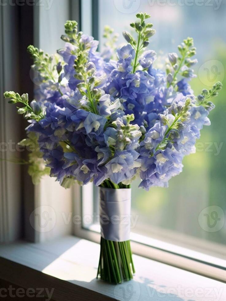 a bouquet of blue flowers in a vase on a window sill by a window