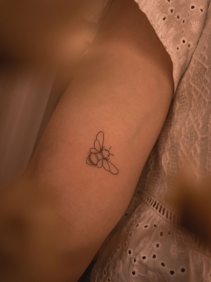 a woman's arm with a small bee tattoo on the left side of her arm