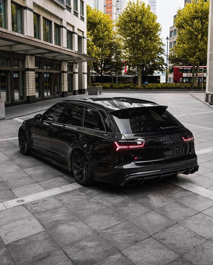 a black car is parked in the middle of a parking lot next to tall buildings