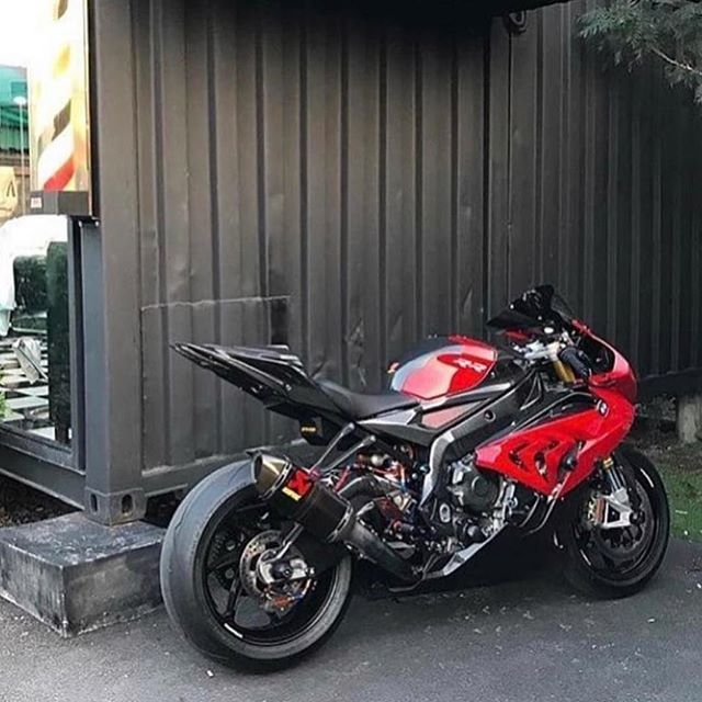 a red and black motorcycle parked in front of a metal building next to a parking meter