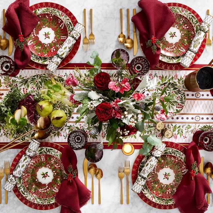 an overhead view of a table setting with red and gold plates, napkins, silverware, and flowers