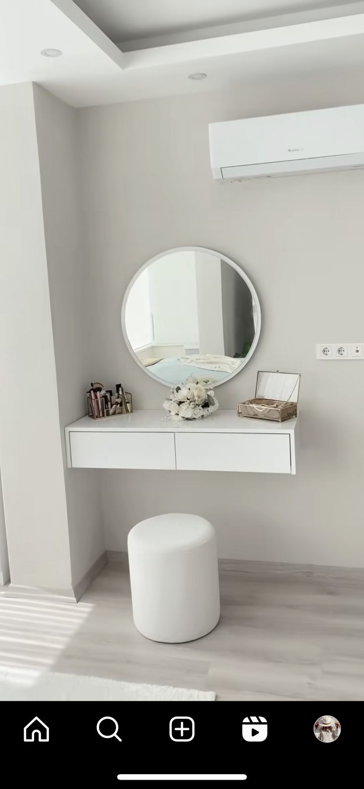 a white vanity with a round mirror above it and a stool in front of it