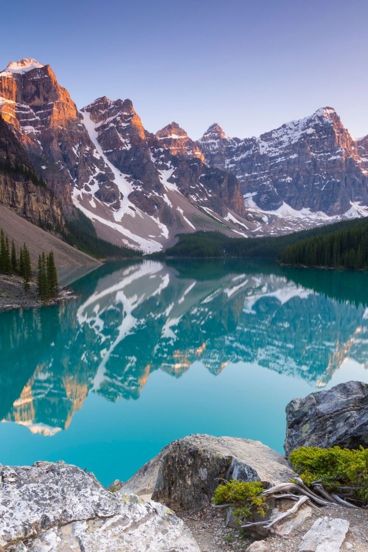 a mountain lake surrounded by snow covered mountains and pine trees in the foreground with blue water