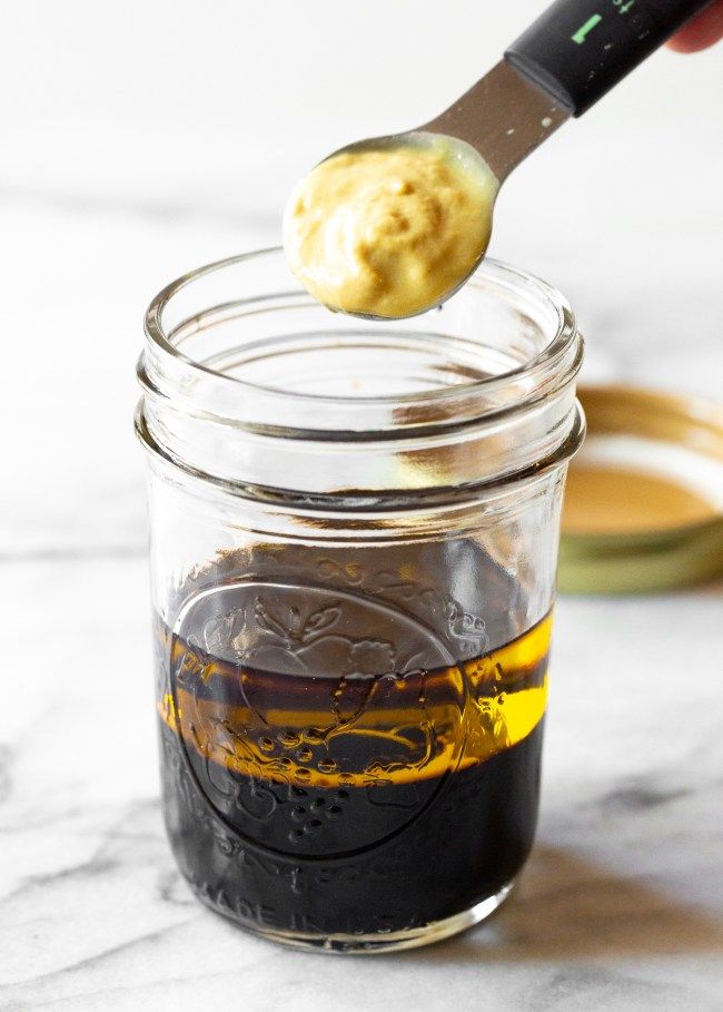 a spoon with some food in it on top of a glass jar filled with liquid