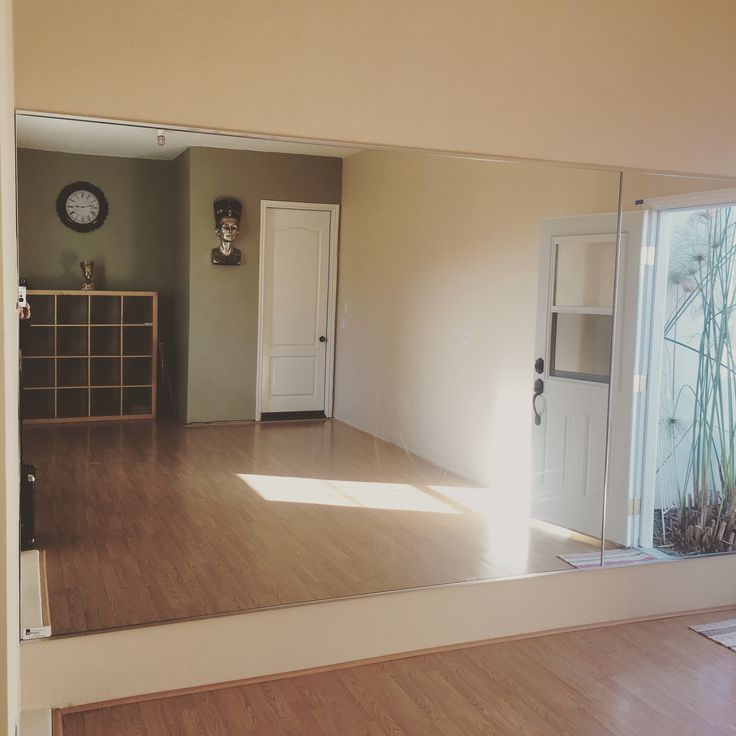 an empty room is reflected in a mirror with a clock on the wall behind it