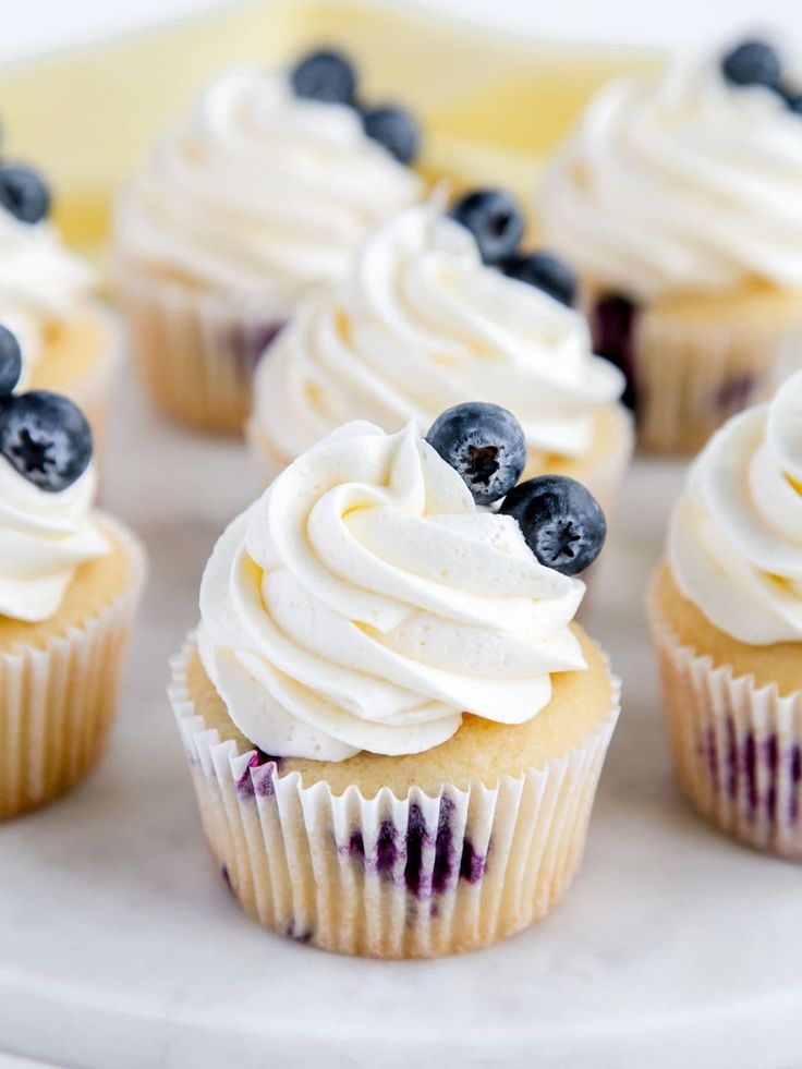 cupcakes with white frosting and blueberries are on a plate, ready to be eaten