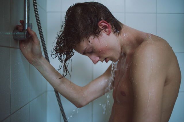 a shirtless man is taking a shower with his head in the air and water coming out of the faucet