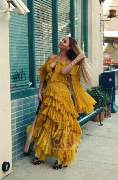 a woman in a yellow dress leaning against a building