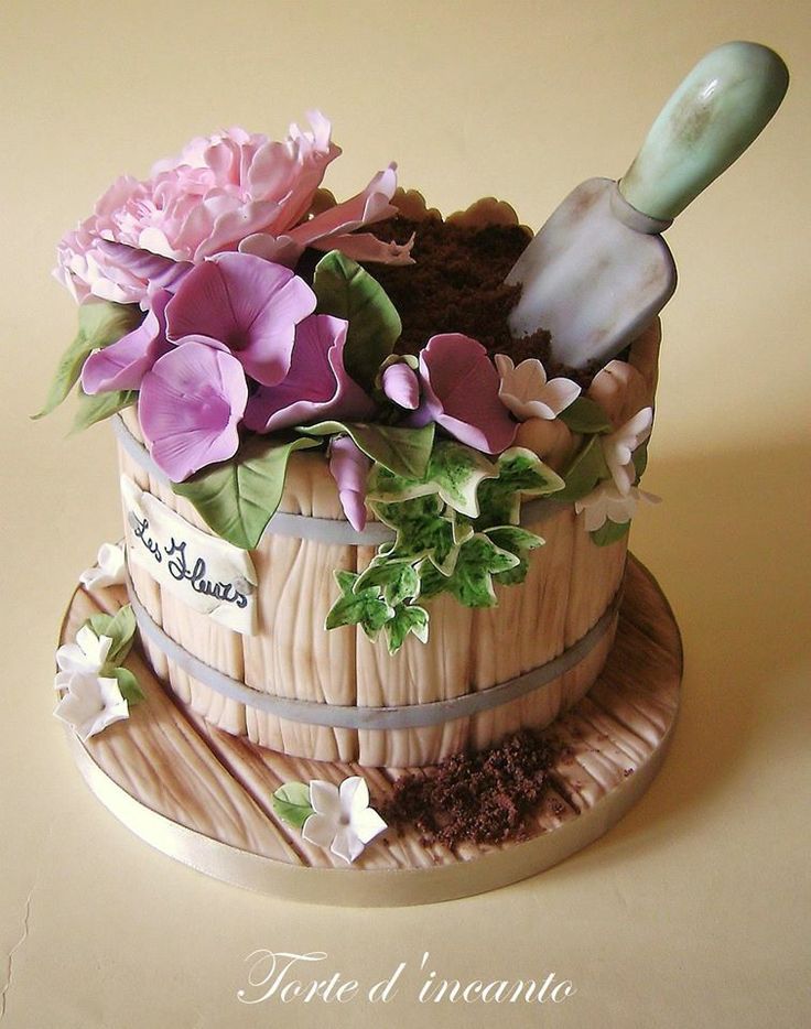 a cake decorated with flowers and gardening utensils in a wooden barrel on a table