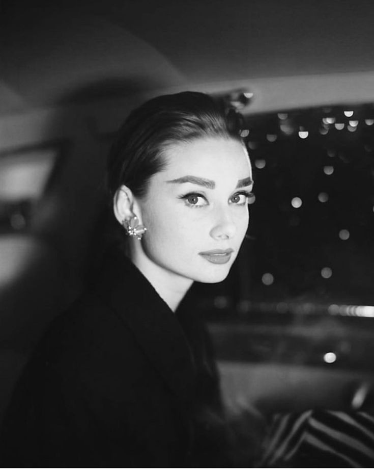 a black and white photo of a woman sitting in a car with city lights behind her