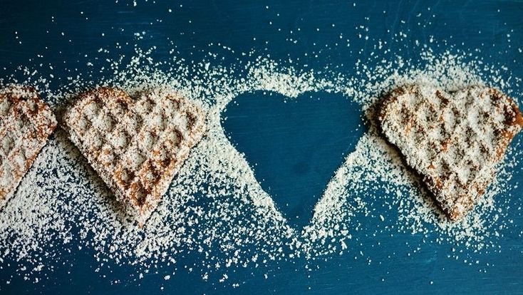 two waffles shaped into the shape of a heart on top of some powdered sugar