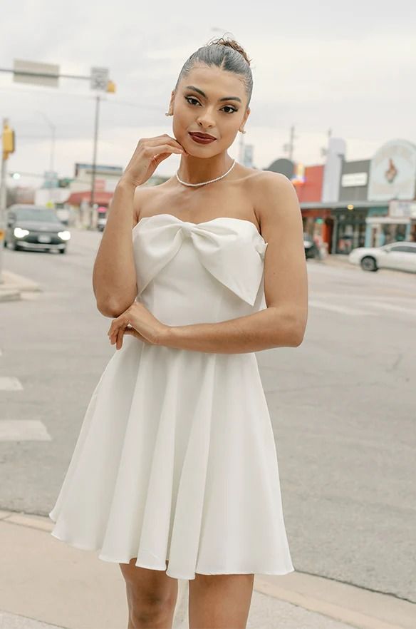 a woman in a short white dress posing on the street with her hand under her chin