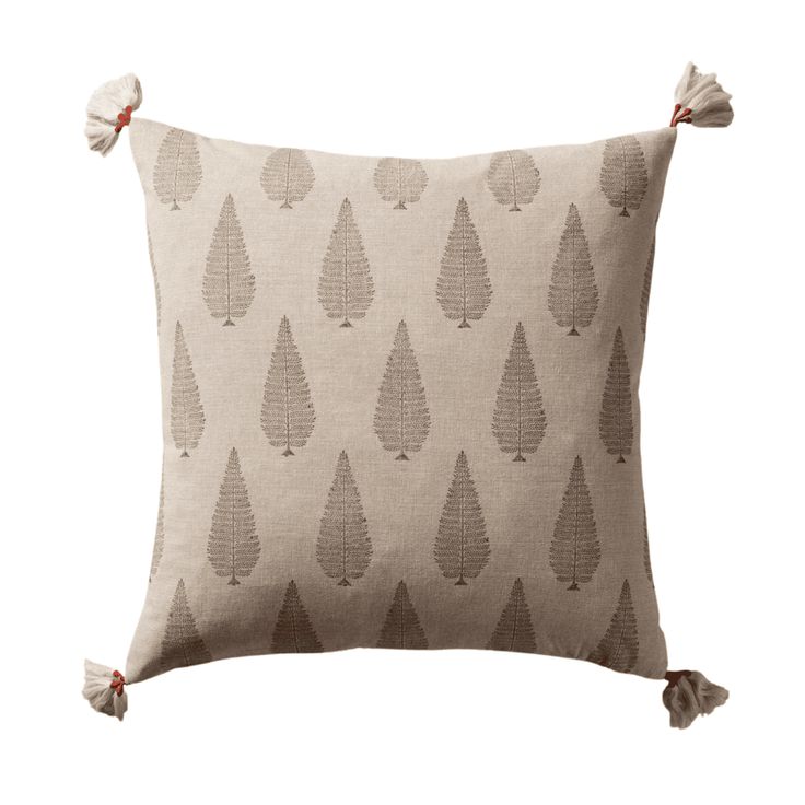 a beige pillow with trees on it and tassels around the edges, in front of a white background